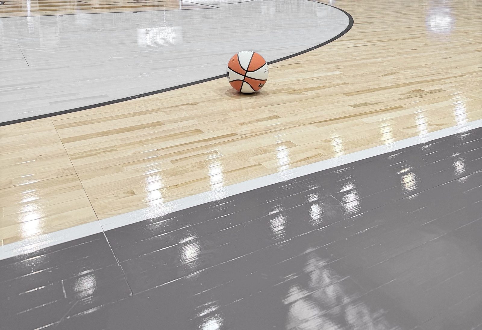 A basketball resting on the hardwood near the court line